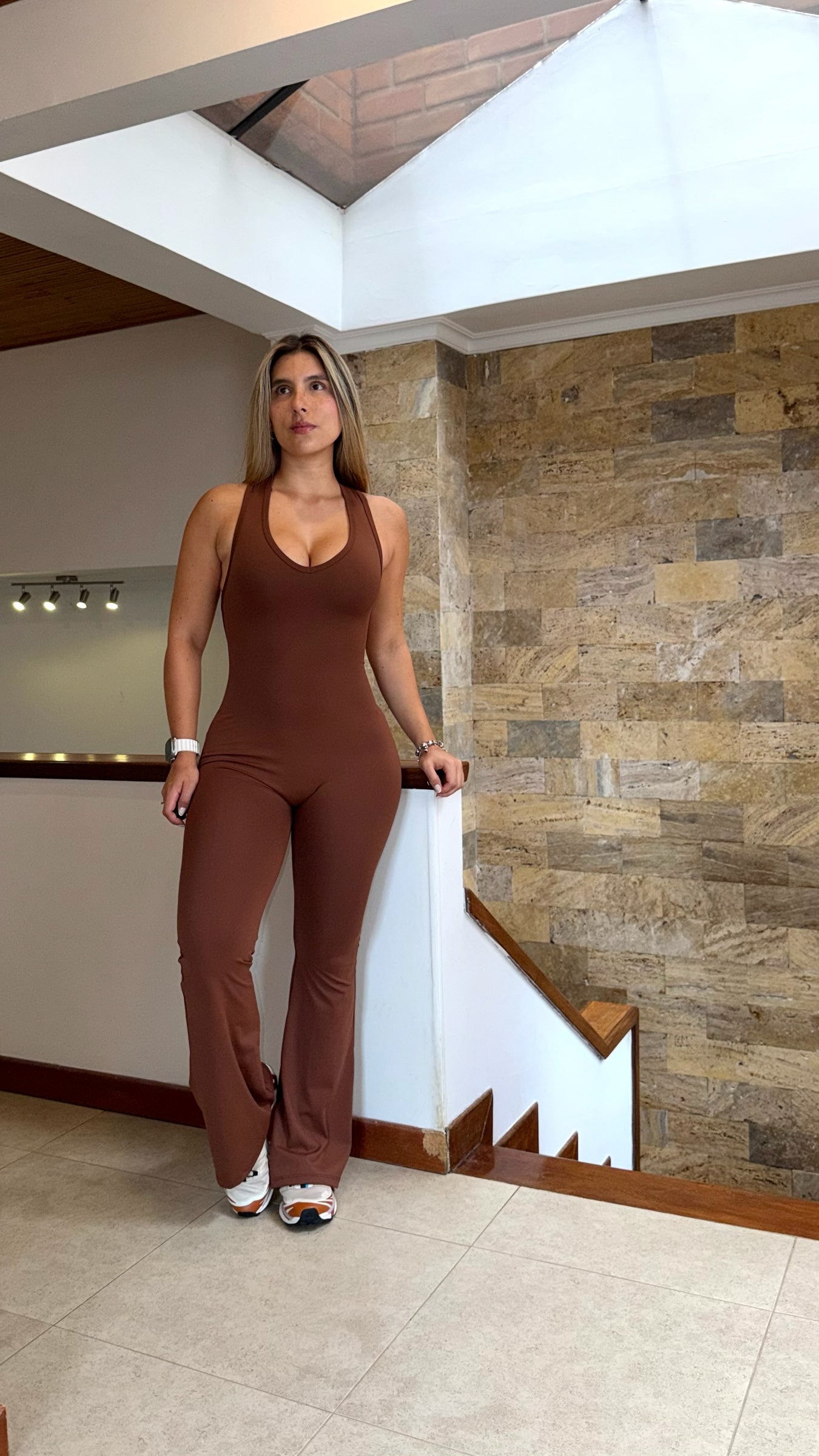 Mujer vistiendo enterizo deportivo largo color café de AMMACTIVE con diseño ajustado y bota campana en interior